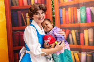 A patient hugging Princess Belle in front of a bookcase backdrop.