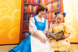 A patient reading a book with Princess Belle in front of a bookcase backdrop.