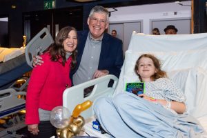 Rick and Rebecca Riordan pose with a patient in a medical bed holding her copy of Percy Jackson and the Olympians.