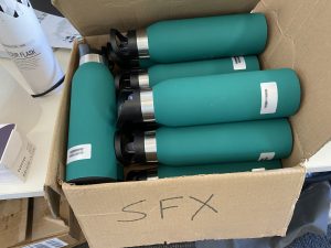 Numerous Teal reusable water bottles sit in a box labeled for the special effects team.