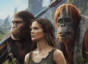 Female character with brown hair from the film stands beside two apes, looking out to something out of frame.