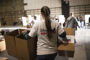 A Disney VoluntEAR carries boxes at a donation drive.