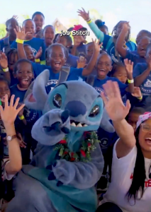Stitches waves to the camera surrounded by school children