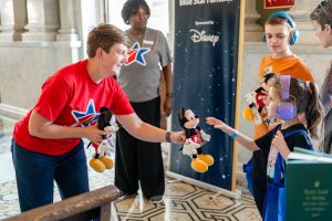 Woman wearing Blue Star Books shirt hands Mickey plush to child