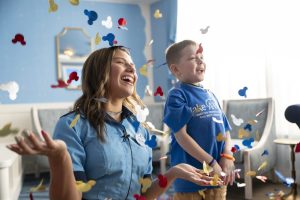 wish kid Paxton smiles with confetti in the air next to wish alumni and cast member Abigail