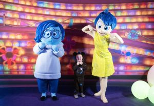 young child poses with Joy and Sadness from Pixar's Inside Out