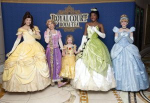 little girl in Belle dress poses with Disney Princesses Belle, Tiana and Cinderella